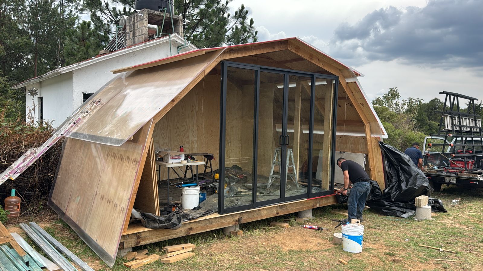 Foto real: la cabaña prototipo en obra, arco de madera en el bosque